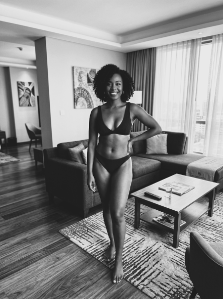 Woman in black lingerie standing in a hotel room.
